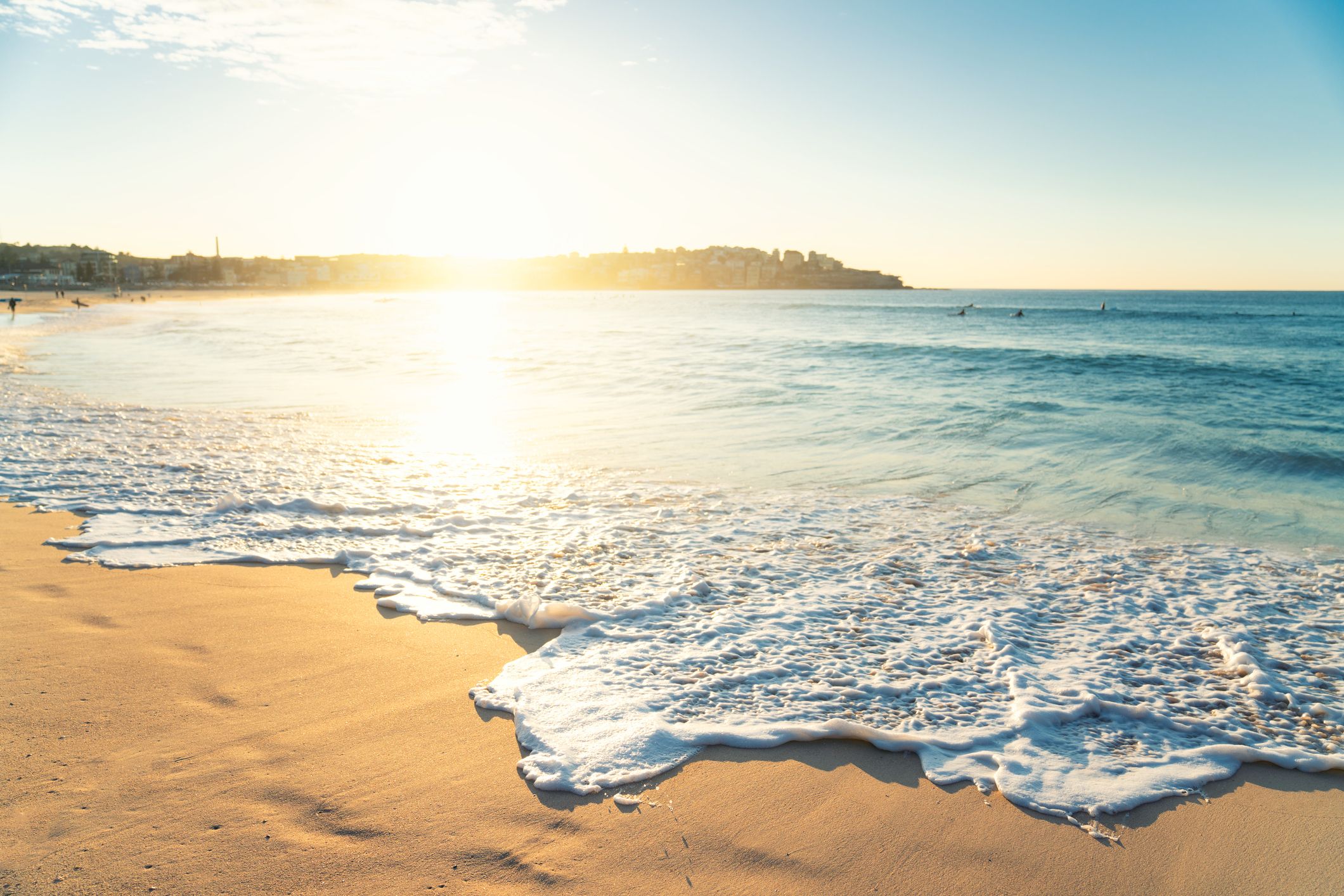 sunray with waves washing onto beach peninsula with houses in the distance