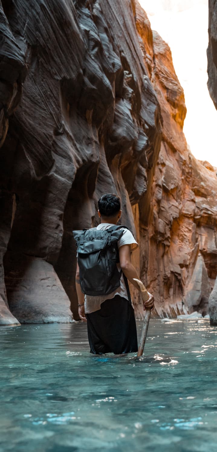man hiking through the narrows water up past his knees hiking pack and stick